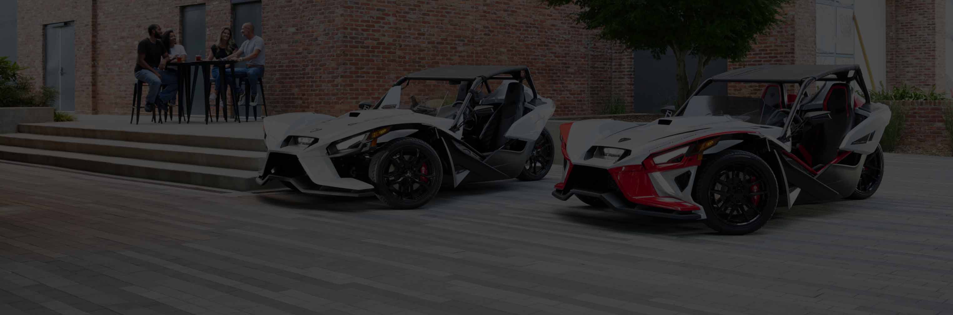 A pair of Slingshot trikes parked outside of an urban area