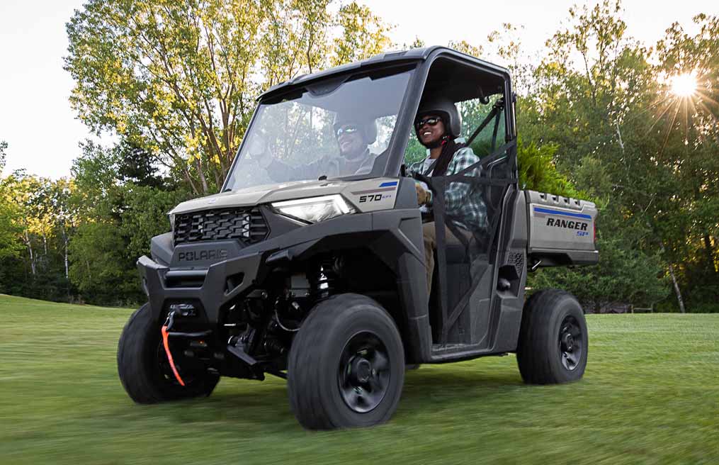 Polaris Ranger with a smiling passenger and driver cruising down a well manicured grass drive