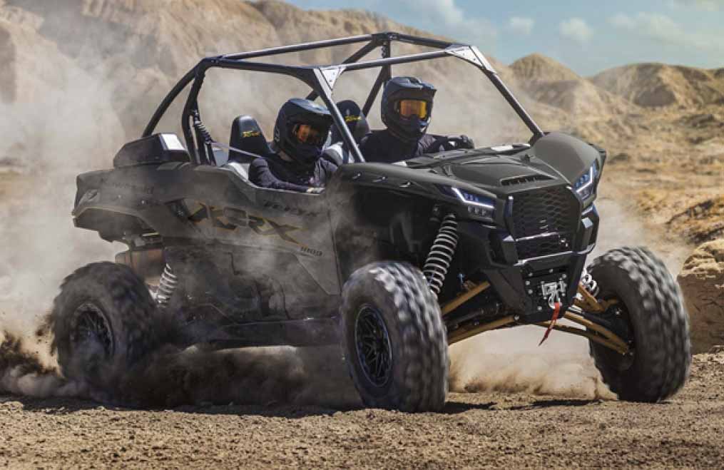 Kawasaki Teryx Side by Side with two riders in it going off road kicking up dust on a sand dune or a beach