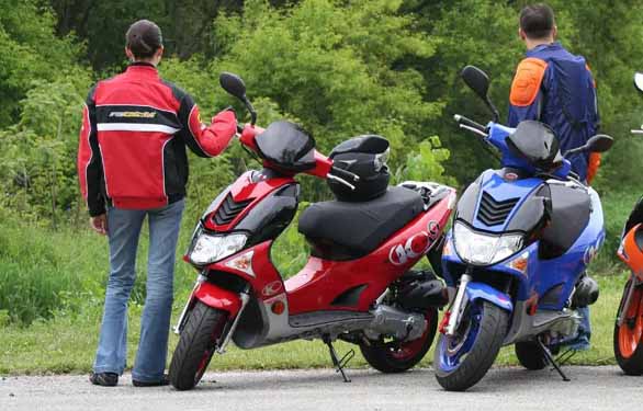 two guys in leather jackets standing next to there Kymco model scooters